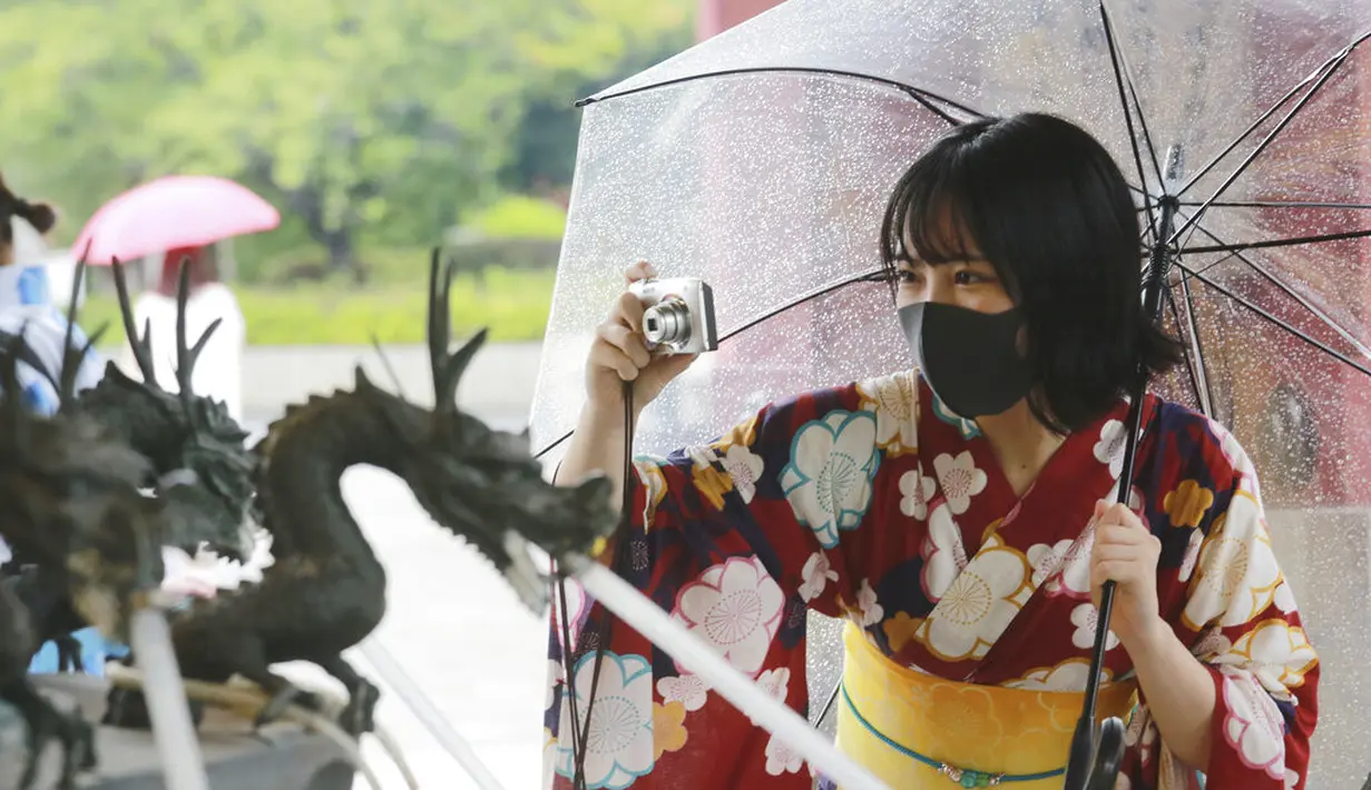 Seorang wanita mengenakan  yukata, pakaian musim panas tradisional Jepang dan masker untuk melindungi diri dari virus corona mengambil foto di lingkungan Asakusa di Tokyo, Jumat (13/8/2021). Yukata adalah jenis kimono yang dibuat dari bahan kain katun tipis tanpa pelapis. (AP Photo/Koji Sasahara)