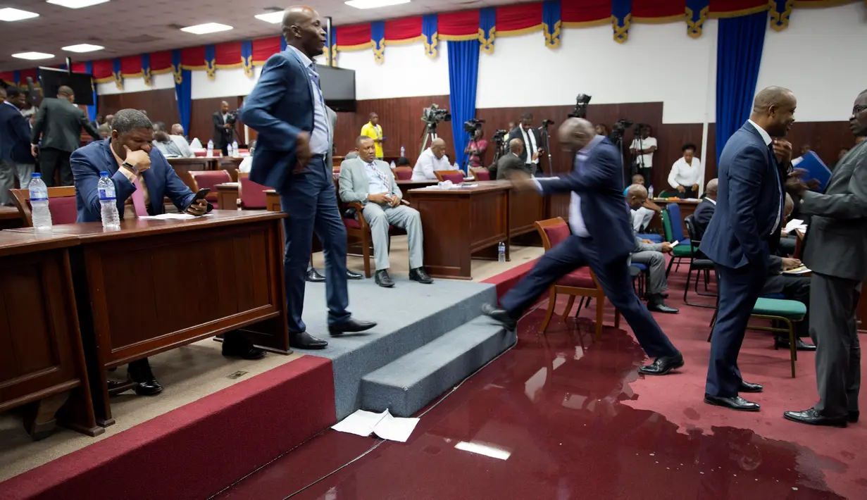 Seorang anggota parlemen melangkahi genangan air hujan pada lantai Gedung Parlemen Haiti di Port-au-Prince, Haiti, Rabu (21/8/2019). Bocornya atap pada Gedung Parlemen Haiti menyebabkan air masuk dan membasahi lantai. (AP Photo/Dieu Nalio Chery)