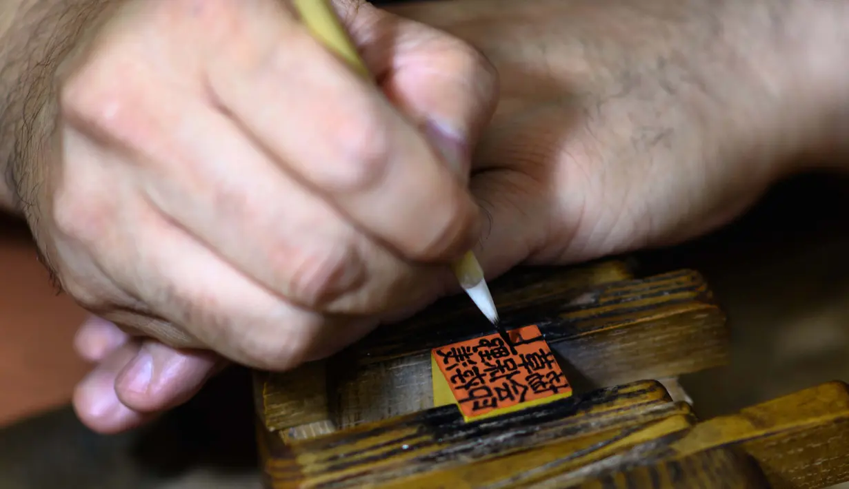 Gambar pada 9 Oktober 2020 menunjukkan pembuat stempel tinta tradisional Takahiro Makino, 44, menulis karakter di saputangan di sebuah studio di Tokyo. Perdana Menteri Yoshihide Suga tengah menggencarkan upaya digitalisasi dan menghapus Hanko atau stempel tinta tradisional Jepang. (Philip FONG/AFP)