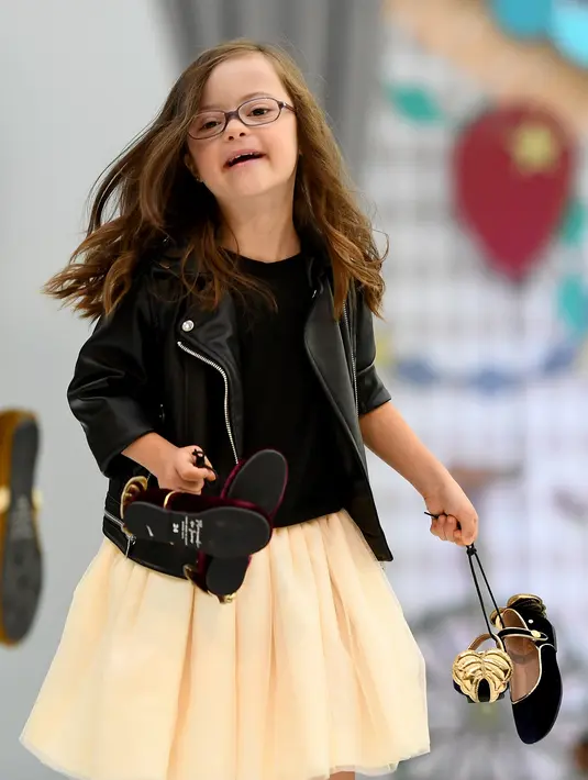 Anak dengan down syndrome menenteng sepatunya sambil berjalan di atas catwalk pada pekan mode Petite Fashion Week di Madrid, 6 Oktober 2017. Penampilan dan gaya model mungil yang menggemaskan dan ekspresif itu sukses mencuri perhatian. (GABRIEL BOUYS/AFP)