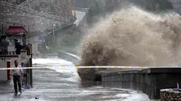 Seorang pria berjalan di dekat ombak besar yang menghantam tembok di pantai dekat Wenling, Provinsi Zhejiang, China, Rabu (11/7). Terpaan Topan Maria menyebabkan ombak besar terjadi di wilayah tersebut. (AFP)