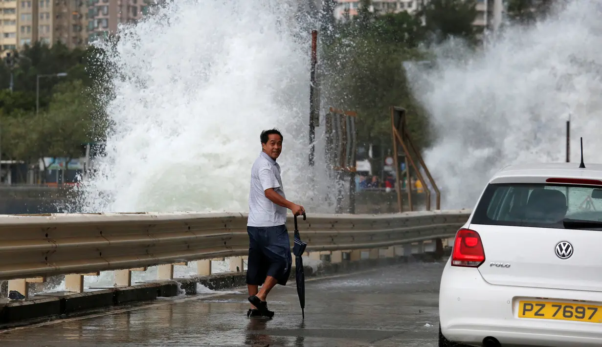 Seorang warga melintas di dekat ombak besar di pesisir Hong Kong, Tiongkok, Jumat (21/10). Banyak warga mengabaikan peringatan dan menyaksikan hantaman ombak besar yang menghantam pesisir tersebut. (REUTERS/Bobby Yip)