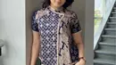 Memadukan kain batik berwarna navy dan coklat susu, membentuk pola geometris dan motif tradisional yang kontras namun harmonis. Potongannya menyerupai kebaya modern berlengan pendek dengan kerah mandarin, dilengkapi kancing depan asimetris yang dihiasi aksen renda atau payet kecil di tepian. (Foto: Instagram @/ligacollection)