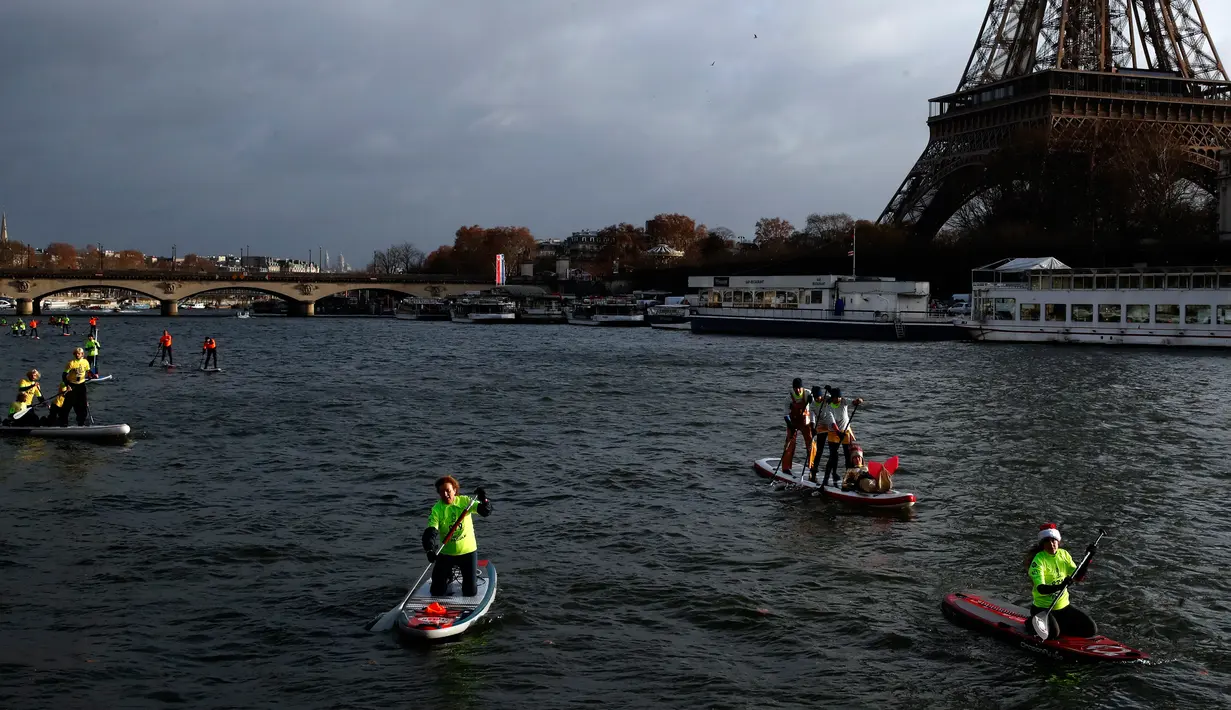Peserta menyeberangi sungai Seine dekat menara Eiffel selama Nautic Paddle Race di Paris, Minggu (9/12). Sekitar 800 orang mengikuti lomba dayung sambil berdiri terbesar di dunia sejauh 11 km dengan pemandangan kota Paris. (AP /Christophe Ena)