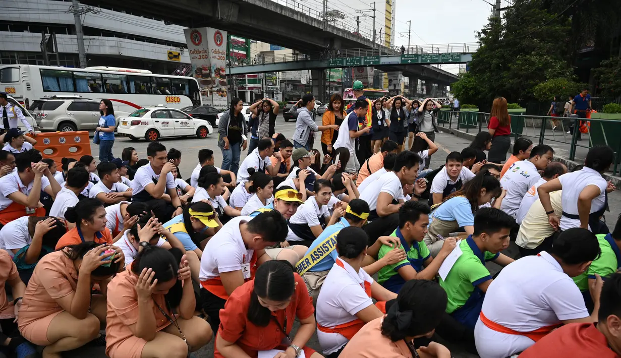 Karyawan pusat perbelanjaan menutupi kepala mereka di sepanjang jalan ketika mereka berpartisipasi dalam latihan gempa di Manila (14/11/2019). Latihan ini sebagai bagian dari kesiapsiagaan nasional menyusul berbagai gempa yang melanda pulau Mindanao bulan lalu. (AFP Photo/Ted Aljibe)