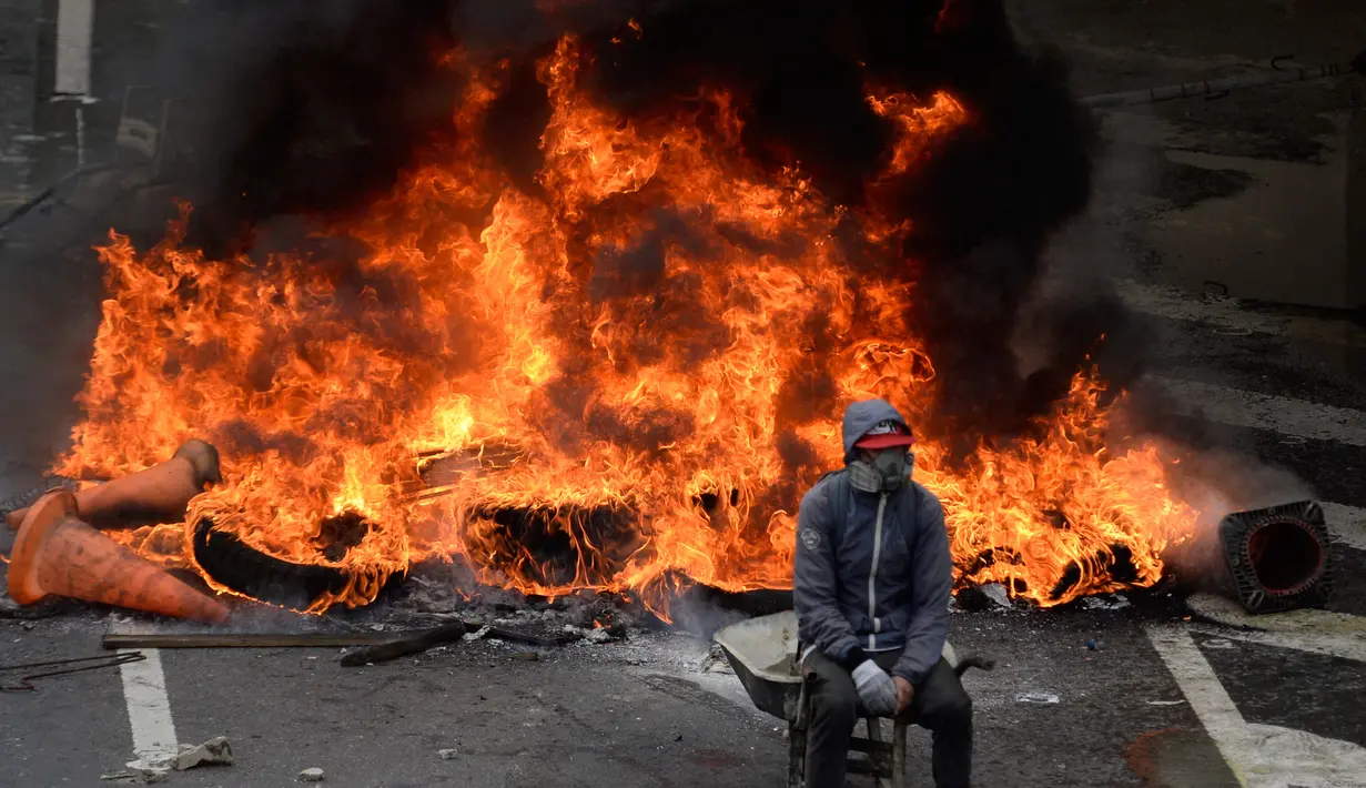 Seorang demonstran dari oposisi Venezuela duduk didepan kobaran api saat menggelar aksinya menentang Presiden Nicolas Maduro di Caracas, Venezuela (24/4). Mereka menggelar protes meminta Presiden Nicolas Maduro untuk mundur. (AFP/Federico Parra)