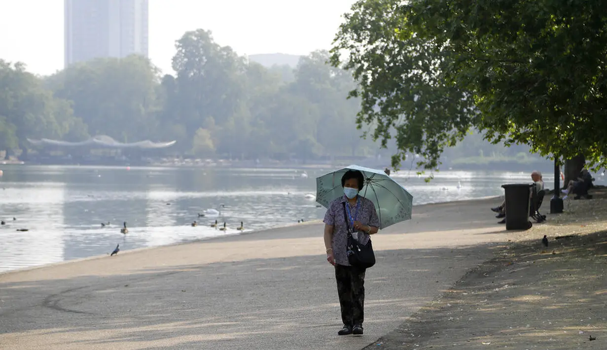 Seorang wanita mengenakan payung saat berjalan di sepanjang The Serpentine di Hyde Park di London, Rabu, (12/8/2020). Peringatan badai masih berlaku untuk sebagian besar Inggris pada hari Rabu, sementara suhu tinggi diperkirakan lagi di banyak bagian Inggris. ( AP Photo / Kirsty Wigglesworth)