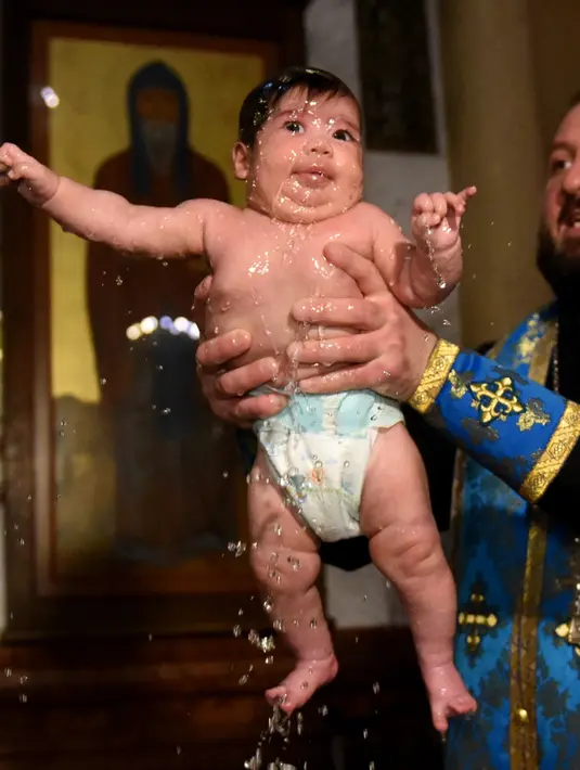 Ekspresi seorang bayi saat pendeta mengangkatnya dari air dalam acara pembaptisan masal di Gereja Katedral Holy Trinity, Tbilisi, Georgia (21/1). (AFP Photo/Vano Shlamov)