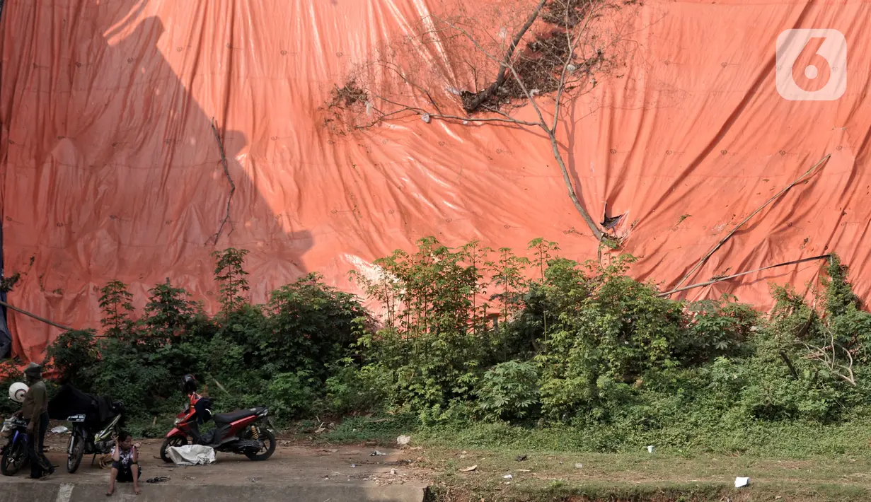 Warga berada dekat lokasi tanah longsor yang ditutupi terpal besar di pinggir Kanal Banjir Timur, Jakarta, Kamis (18/6/2020). Warga setempat mengaku khawatir terjadi longsor susulan karena terpal dan karung pasir yang digunakan untuk menutupi lokasi longsor kian rapuh. (merdeka.com/Iqbal S. Nugroho)