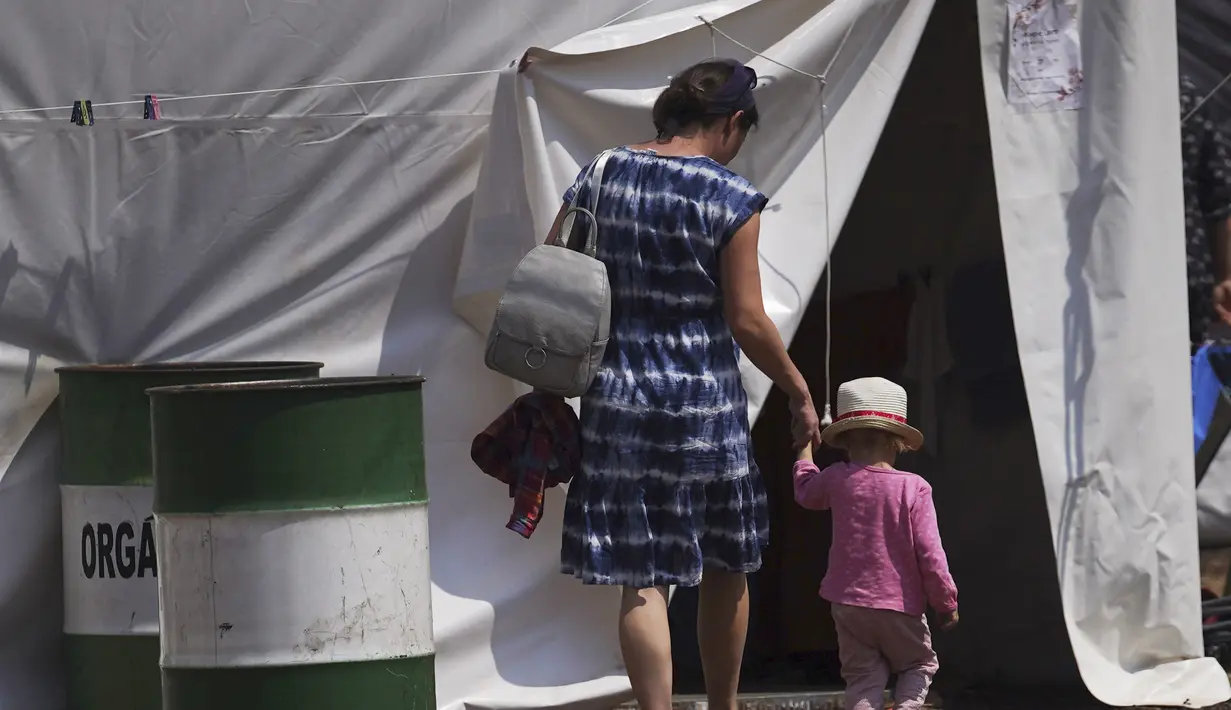 <p>Seorang ibu Ukraina dan anaknya berjalan bergandengan tangan ke dalam tenda di sebuah kamp pengungsi di wilayah Iztapalapa, Mexico City, Selasa (24/5/2022). Mexico City akan menutup kamp yang telah menampung ratusan pengungsi Ukraina selama sebulan terakhir setelah program AS mengizinkan mereka terbang ke Negeri Paman Sam sudah beroperasi dan pihak berwenang mengatakan kamp itu tidak lagi diperlukan. (AP/Marco Ugarte)</p>