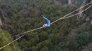 Kontestan berpakaian karakter Avatar bergaya saat melintasi slackline di Pegunungan Huangshizhai di Zhangjiajie, Hunan, China, Minggu (23/12). Pemandangan tersebut memberi sensasi bukit-bukit yang melayang, persis di film Avatar. (STR/AFP)