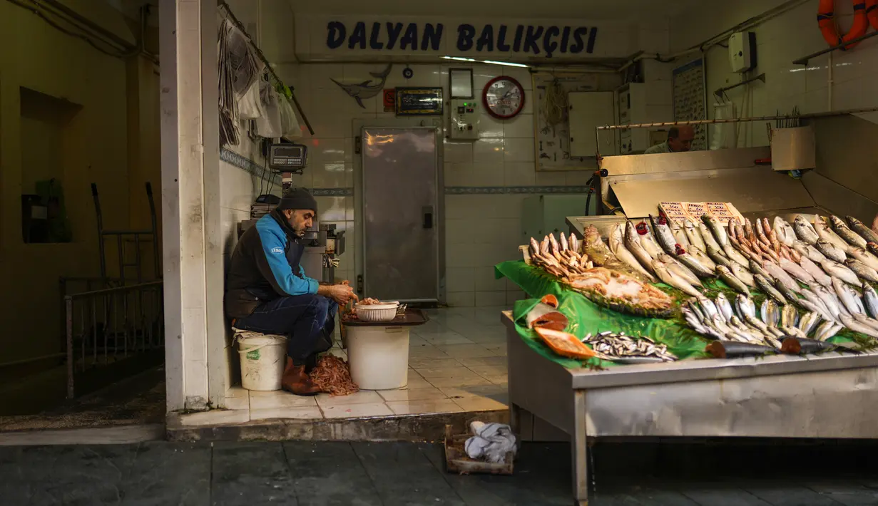 Seorang penjual ikan mengupas udang saat menunggu pembeli di pasar jalanan di Istanbul, Turki, Senin (3/1/2022). Inflasi tahunan Turki naik dengan laju tercepat dalam 19 tahun, melonjak menjadi 36,08% pada Desember lalu, menurut data resmi pada Senin. (AP Photo/Francisco Seco)