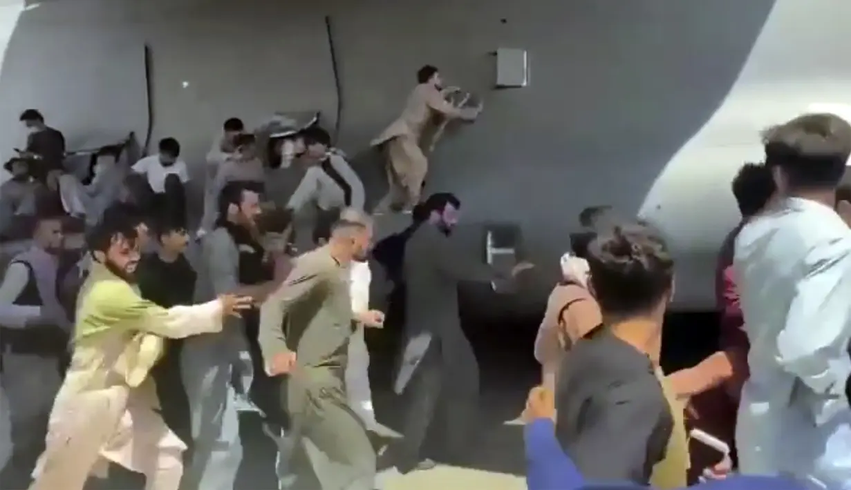Ratusan orang berusaha menaiki pesawat angkut C-17 Angkatan Udara AS di landasan bandara internasional, di Kabul, Afghanistan (16/8/2021).  Di tengah kekacauan pasca direbutnya Ibukota Kabul oleh pasukan Taliban, dua warga jatuh dari pesawat militer Amerika Serikat. (Verified UGC via AP)