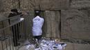 Pekerja memindahkan catatan doa yang ditinggalkan pengunjung dari celah di antara batu-batu di Tembok Barat, situs paling suci tempat orang Yahudi dapat berdoa di Kota Tua Yerusalem, Selasa, 20 September 2022, menjelang Rosh Hashana, Tahun Baru Yahudi. Catatan dimakamkan di pemakaman terdekat menurut tradisi Yahudi. Operasi dilakukan dua kali setahun sebelum Rosh Hashana dan sebelum liburan Paskah di musim semi. (AP/Mahmoud Illean)