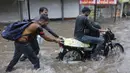 Dua pria membantu seorang pengendara motor menerobos jalan yang tergenang air setelah hujan lebat akibat siklon Tauktae di Ahmedabad, India, Selasa (18/5/2021). Topan Tauktae disebut yang terbesar melanda wilayah itu dalam beberapa dekade terakhir.  (AP Photo/Ajit Solanki)