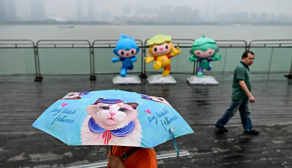 Seorang wanita yang membawa payung berjalan melewati maskot Asian Games 2022, Chenchen, Congcong, dan Lianlian, di sepanjang jalur pejalan kaki sungai Qiantang di Hangzhou, provinsi Zhejiang, China, pada 22 September 2023. (MANAN VATSYAYANA/AFP)
