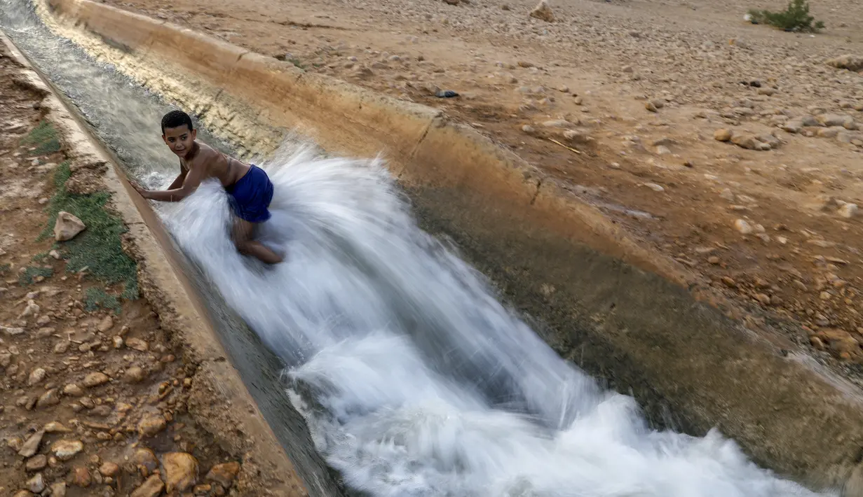 Seorang anak bermain di aliran mata air yang digunakan untuk irigasi untuk mendinginkan tubuh saat suhu udara mencapai 44 derajat Celcius di kota Jericho, Tepi Barat (1/9/2020). (AFP Photo/Ahmad Gharabli)