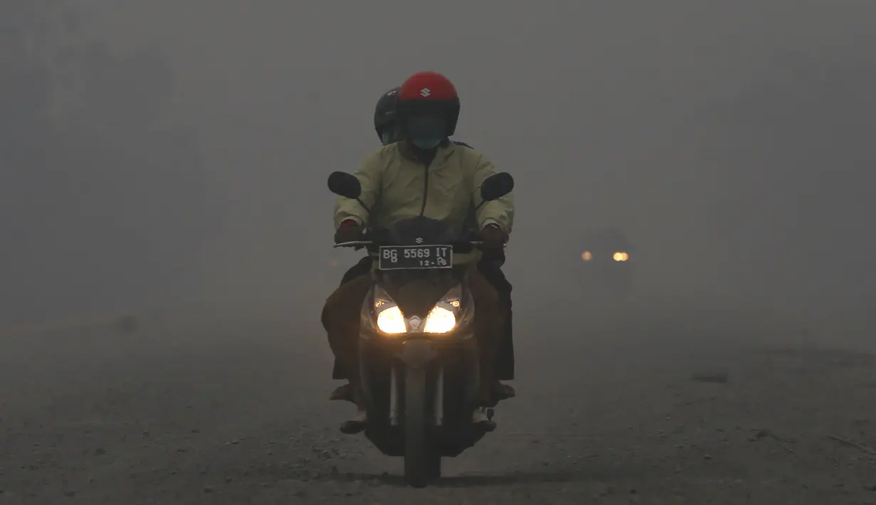 Pengendara motor menerobos jalan berkabut asap di jalan dekat pelabuhan Tanjung Siapi Api, Palembang, Sabtu (19/9/2015). Kabut asap akibat kebakaran hutan ini sangat membahayakan kesehatan dan keselamatan. (Reuters/Beawiharta)