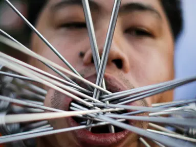 Seorang pemuja dari Kuil Samkong menusukkan besi ke pipi saat memeriahkan festival vegetarian di Phuket, Thailand (4/10). Festival ini menampilkan aksi ekstrem pemuja dengan menusukkan benda tajam ke wajah. (REUTERS/Jorge Silva)
