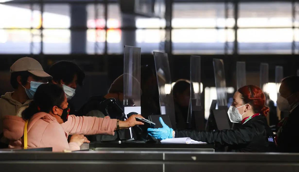 Traveler menyerahkan paspor kepada agen maskapai saat check in di terminal internasional Bandara Los Angeles (LAX), Selasa (21/12/2021). AAA memperkirakan lebih dari 109 juta orang Amerika akan melakukan perjalanan pada musim liburan, meningkat 27,7% dari tahun 2020. (MARIO TAMA/Getty Images via AFP
