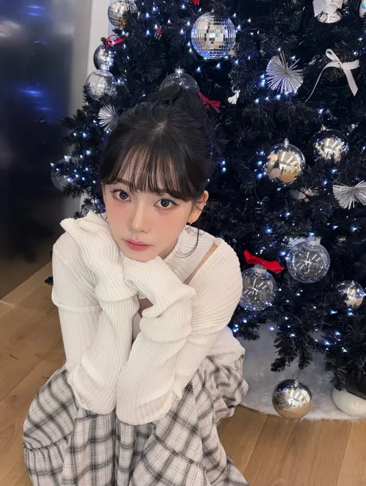 Karina aespa berfoto di pohon Natal dengan ornamen silver. Ia tampil mengenakan knit top putih cut out di bagian merah dipadukan rok panjang tartan. [@katarinabluu]