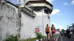 Dua turis asing berjalang di sepanjang dinding parimeter Lembaga Pemasyarakatan (Lapas) Kerobokan, Bali, Senin (19/6). Empat narapidana asing kabur melalui lubang sepanjang 15 meter yang mengarah ke parit di luar bangunan Lapas. (SONNY TUMBELAKA/AFP)
