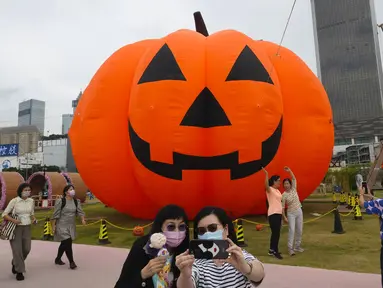 Seorang wanita mengenakan masker untuk mencegah penyebaran virus corona, berpose untuk selfie di depan dekorasi buah labu besar untuk Halloween di sebuah taman di Hong Kong, Rabu (27/10/2021). Tahun ini, perayaan tersebut jatuh pada hari Minggu, 31 Oktober 2021. (AP Photo/Vincent Yu)