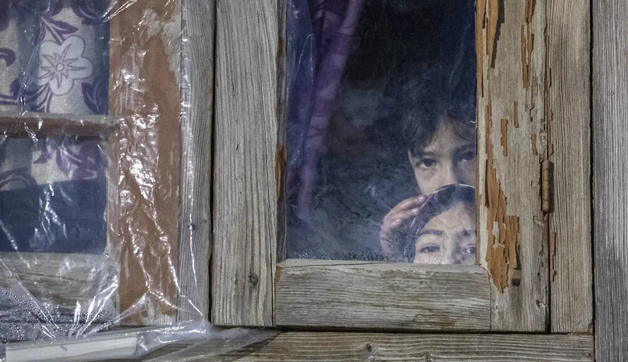 Anak-anak melihat dari balik jendela rumah mereka yang tertutup saat operasi kontra-pemberontakan di pinggiran Srinagar, Kashmir, India, 3 Januari 2022. Menurut polisi, seorang pemberontak utama dan rekannya tewas dalam operasi tersebut. (AP Photo/Mukhtar Khan)