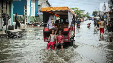 Anak-anak duduk di belakang kendaraan yang melintas saat banjir rob di Muara Angke, Jakarta, Jumat (25/11/2022). Badan Penanggulangan Bencana Daerah (BPBD) DKI Jakarta mengimbau agar warga di pesisir Jakarta mengantisipasi banjir pesisir atau rob selama 22-28 November 2022. (Liputan6.com/Faizal Fanani)