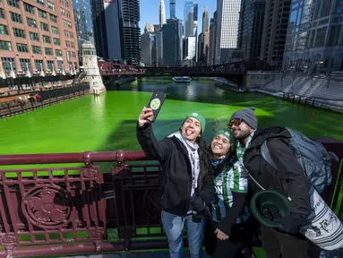 Sekelompok orang berselfie dengan latar belakang Sungai Chicago yang berwarna hijau di LaSalle Street Bridge, Sabtu (12/3/2022). Perubahan warna ini dilakukan untuk menyambut Hari St. Patrick pada Kamis mendatang. (Tyler Pasciak LaRiviere/Chicago Sun-Times via AP)