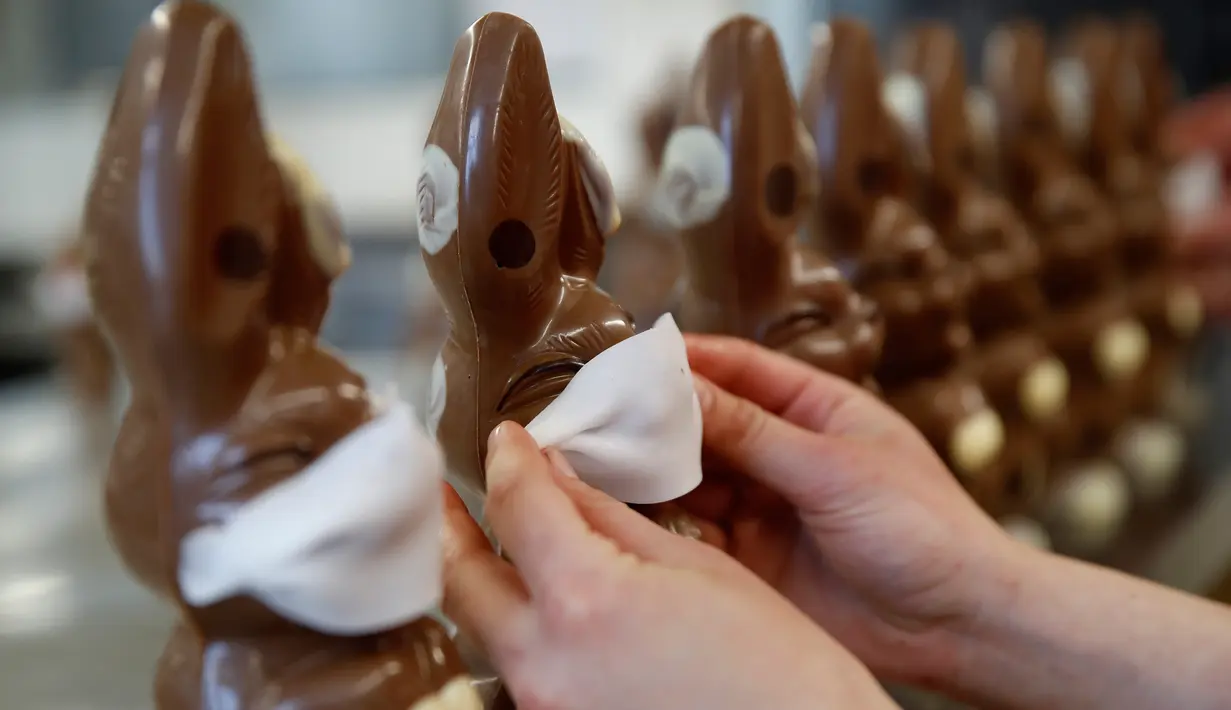 Pekerja menyiapkan cokelat paskah berbentuk kelinci yang mengenakan masker di toko roti Baeckerei Bohnenblust di Bern, Swiss, Jumat (27/3/2020). Cokelat paskah yang dibuat di tengah pandemi virus corona yang sedang merebak di seluruh dunia ini dijual sekitar RP 143 ribu. (STEFAN WERMUTH/AFP)