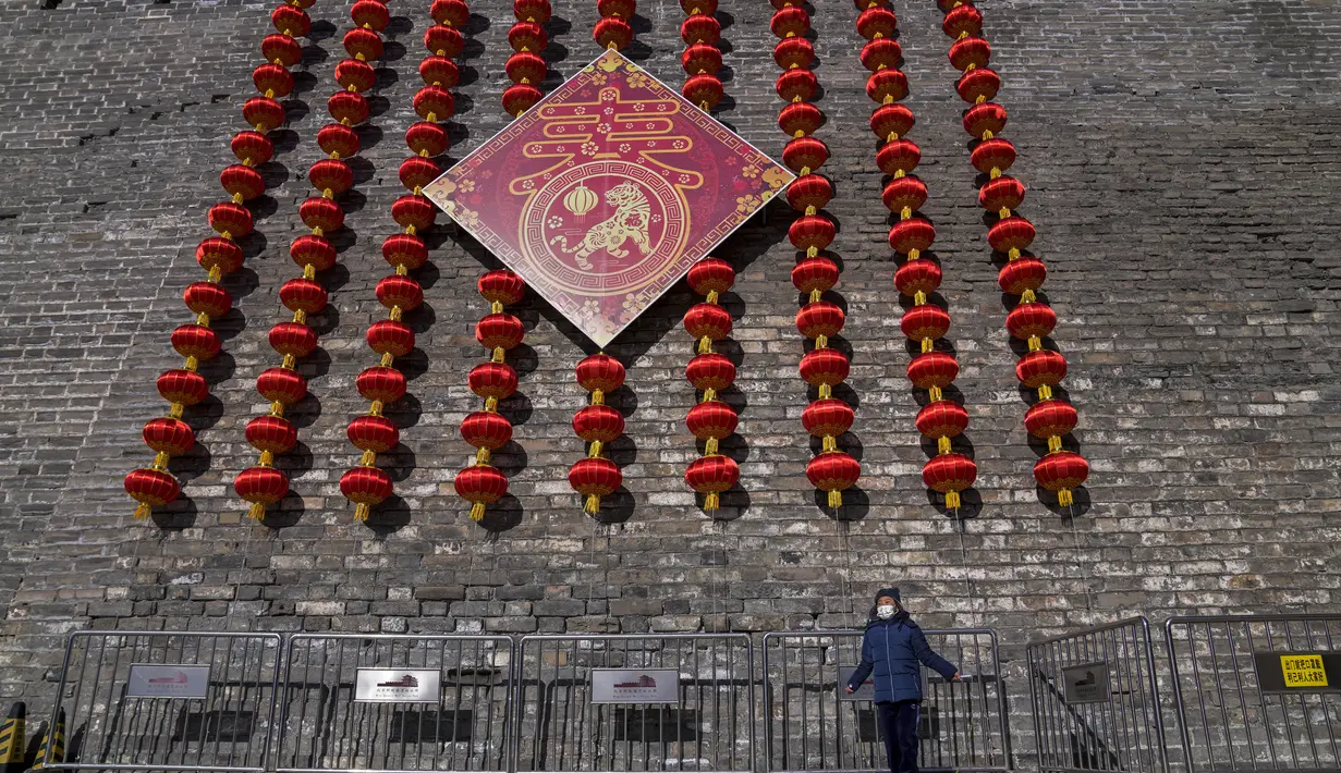 Seorang anak mengenakan masker untuk membantu melindungi dari virus corona bermain lompat tali di dekat dekorasi lentera untuk Tahun Baru Imlek mendatang di sisa-sisa tembok kota di Beijing, Kamis (27/1/2022). (AP Photo/Andy Wong)