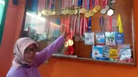 Siti Aisah, ibunda lifter Windy Cantika Aisah, memamerkan medali prestasi putrinya. (Bola.com/Erwin Snaz)