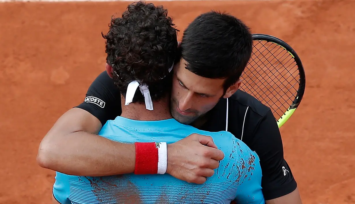 Petenis Serbia, Novak Djokovic memeluk petenis Italia Marco Cecchinato seusai perempatfinal Prancis Terbuka 2018 di stadion Roland Garros, Selasa (5/6). Djokovic tumbang 3-6, 6-7, 6-1, dan 6-7 dalam waktu 3 jam 26 menit. (AP Photo/Michel Euler)