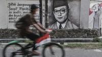 Pesepeda melintasi mural bergambar sosok Bung Hatta di Jalan Pluit Raya III, Jakarta, Minggu (10/8/2020). Mural itu diharapkan menjadi media agar masyarakat selalu mengingat sejarah dan menghargai jasa para pahlawan dalam memerdekakan Tanah Air. (merdeka.com/Iqbal Nugroho)