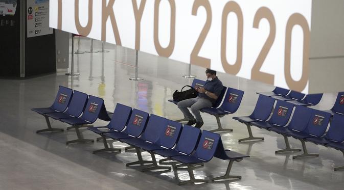 Sorang pria yang mengenakan masker pelindung untuk membantu mengekang penyebaran virus corona berhenti di dekat spanduk Olimpiade Tokyo 2020 di Bandara Internasional Narita, Tokyo, Selasa siang (1/6/2021). (AP Photo/Eugene Hoshiko)