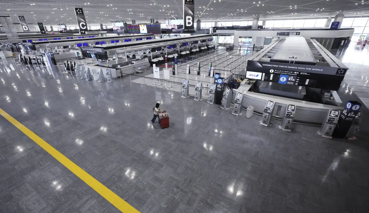 Seorang penumpang yang mengenakan masker pelindung untuk membantu mengekang penyebaran virus corona berjalan di area tiket kosong di Bandara Internasional Narita, Tokyo, Selasa siang (1/6/2021). (AP Photo/Eugene Hoshiko)