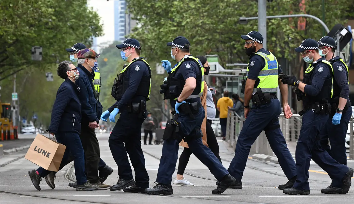 Orang-orang membawa belanjaan mereka saat polisi berpatroli di Melbourne, Australia, Kamis (30/9/2021). Melbourne bergulat dengan lonjakan infeksi Covid-19 di mana sebanyak 1.438 kasus dilaporkan, jumlah harian terbesar sejak awal pandemi. (William WEST / AFP)