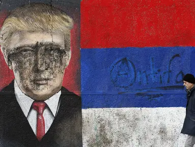 Seorang pria melintas di depan grafiti bergambar Presiden AS terpilih Donald Trump yang dirusak dengan cat di Belgrade, Serbia, Jumat (20/1). Trump hari ini akan dilantik menjadi Presiden AS. (AP Photo / Darko Vojinovic) 