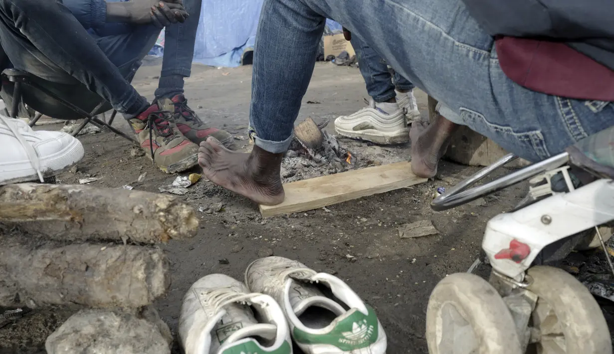 Seorang migran menghangatkan kakinya di kamp darurat di luar Calais, Prancis utara, Sabtu (277/11/2021). Di kamp-kamp darurat di luar Calais, para migran yang putus asa menunggu kesempatan untuk mencoba menyeberangi Selat Inggris. (AP Photo/Rafael Yaghobzadeh)