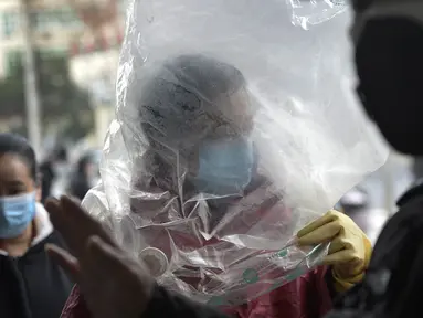 Seorang pria menutupi dirinya dengan plastik pelindung sebelum memasuki sebuah supermarket di Wuhan di provinsi Hubei, China tengah, Senin, (10/2/2020). China melaporkan kenaikan angka kematian akibat wabah virus corona. (Chinatopix via AP)