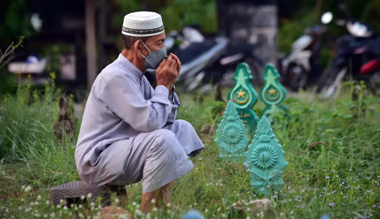 Seorang pria berdoa di sebelah makam kerabat saat perayaan Hari Raya Idul Adha di sebuah pemakaman di Provinsi Narathiwat, Thailand, Rabu (21/7/2021). Setiap Idul Adha atau hari besar Islam lainnya, sebagian warga banyak mendatangi kuburan untuk mendoakan keluarganya. (Madaree TOHLALA/AFP)