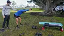 Seorang trainer menyaksikan anggota fitness berolahraga di sebuah taman di pinggiran timur Sydney, pada 14 September 2021. Pelatih pribadi telah mengubah taman kawasan tepi laut di Rushcutters Bay menjadi gym luar ruangan untuk menyiasati pembatasan lockdown karena pandemi covid-19. (AP/Mark Baker)