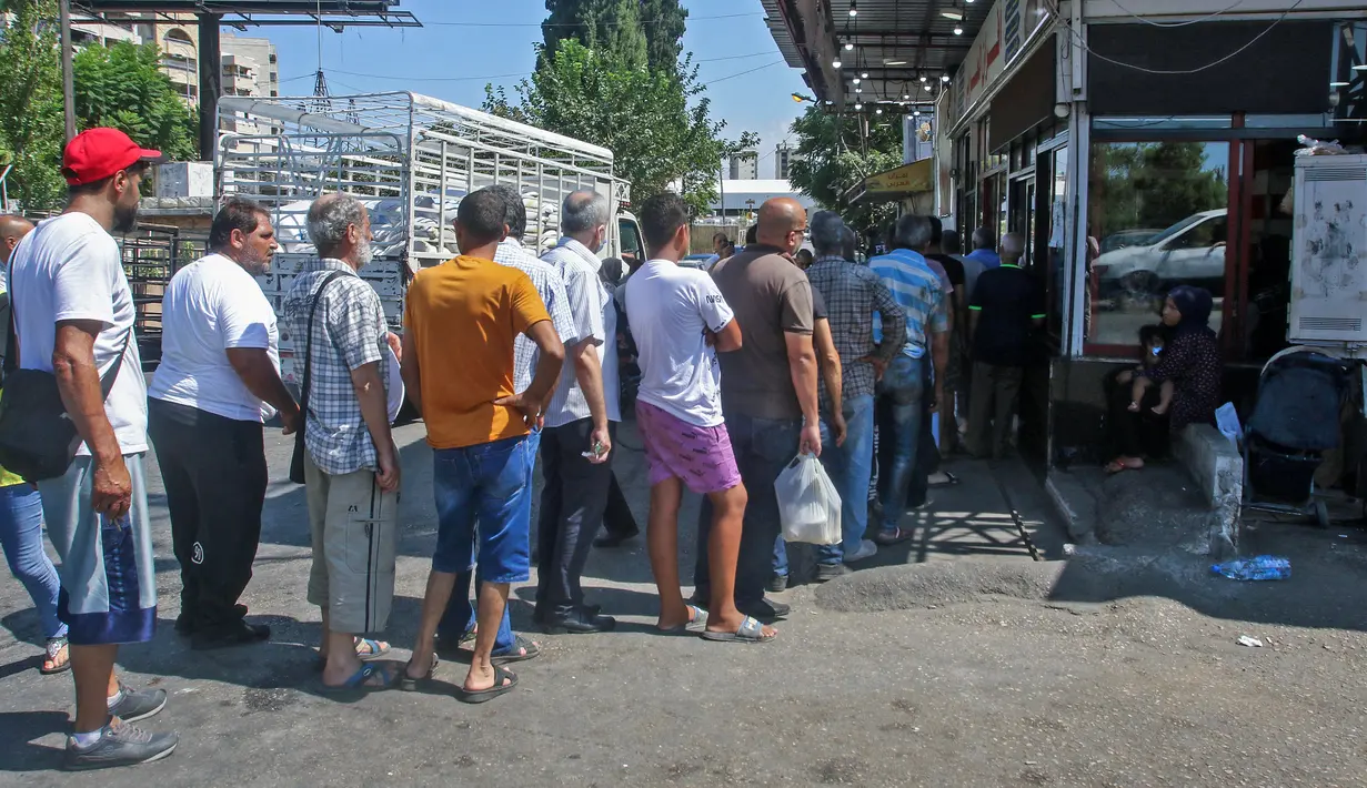 Warga Lebanon antre roti di depan toko roti di kota pesisir selatan Sidon, Jumat (13/8/2021). Tanpa masker, warga Lebanon berbondong-bondong ke toko roti sebelum fajar untuk membeli roti yang terjangkau di tengah krisis ekonomi parah yang memicu berbagai kelangkaan bahan pokok. (Mahmoud ZAYYAT/AFP)