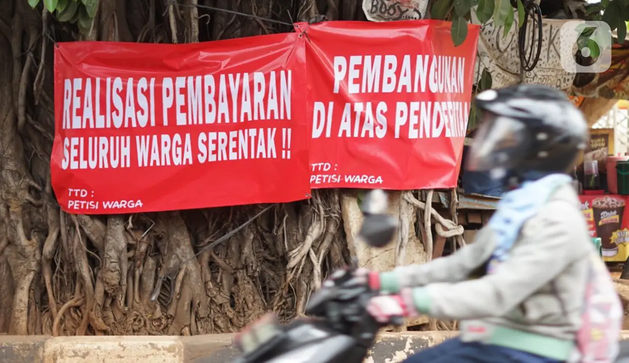 Pengendara motor melintas di depan poster protes warga terhadap pembangunan flyover di kawasan Tanjung Barat, Jakarta, Rabu (15/7/2020). Dalam poster protes tersebut, warga menuntut agar pembayaran pelunasan pembebasan lahan segera diselesaikan secara serentak. (Liputan6.com/Immanuel Antonius)