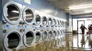 Pamela Cerruti berjalan melewati Pajaro Coin Laundry saat banjir mengelilingi mesin-mesin di komunitas Pajaro di Monterey County, California, Selasa, 14 Maret 2023.  (AP Photo/Noah Berger)