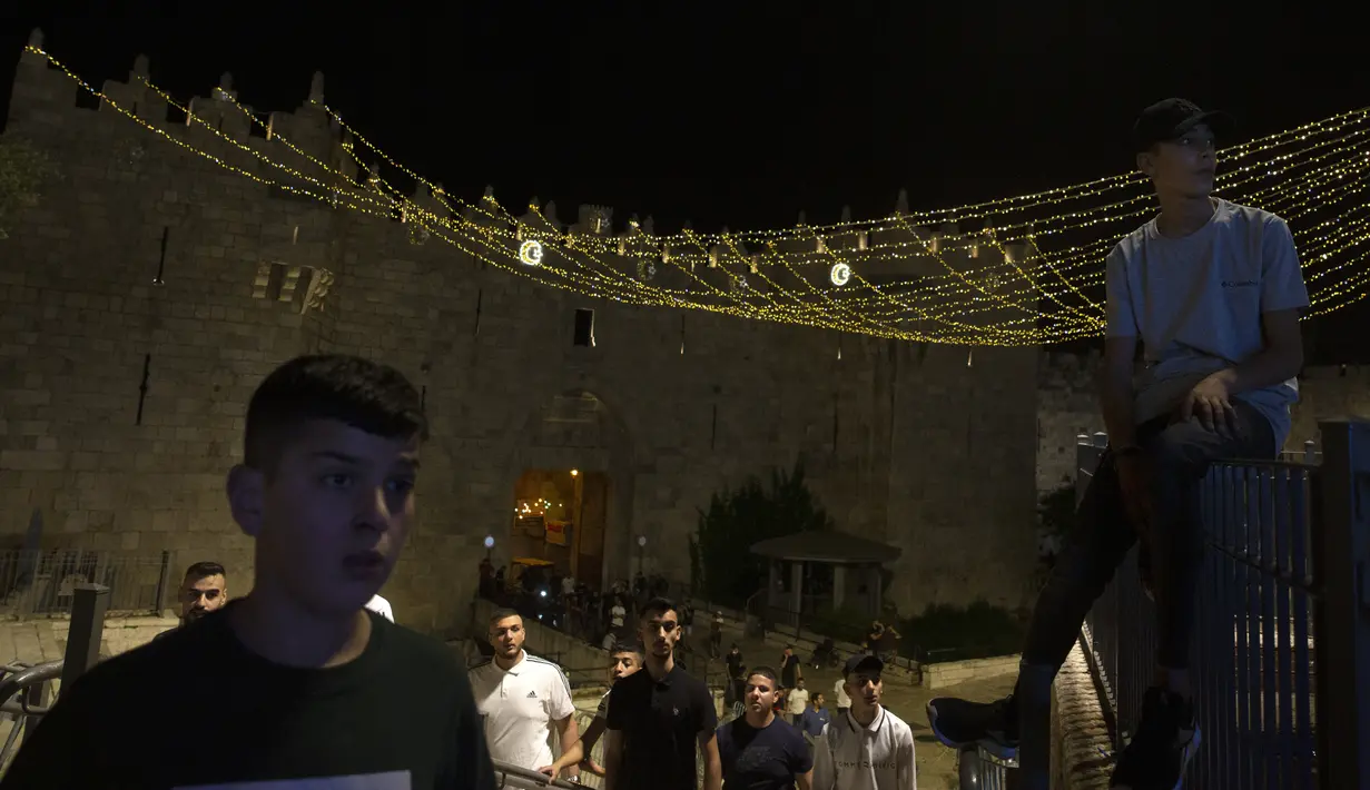 Pemuda Palestina berkumpul di dekat Gerbang Damaskus ke Kota Tua Yerusalem saat mereka menyaksikan polisi Israel membubarkan kerumunan selama bulan suci Ramadhan, Senin (19/4/2021). Bentrokan serupa terjadi setiap malam sejak Ramadhan dimulai pekan lalu. (AP Photo/Maya Alleruzzo)