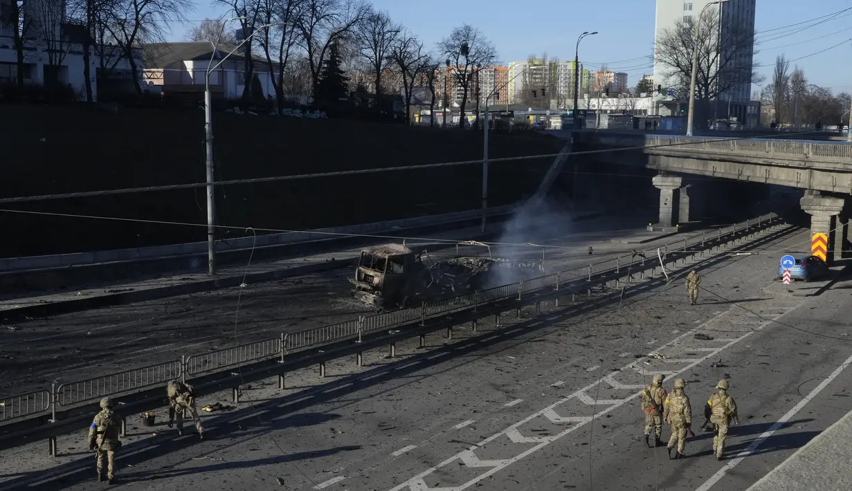 Tentara Ukraina berjalan di dekat puing-puing truk militer yang terbakar di sebuah jalan di Kyiv, Ukraina, Sabtu (26/2/2022). Pasukan Rusia menyerbu ke arah ibukota Ukraina Sabtu, dan pertempuran jalanan pecah saat pejabat kota mendesak penduduk untuk berlindung. (AP Photo/Efrem Lukatsky)