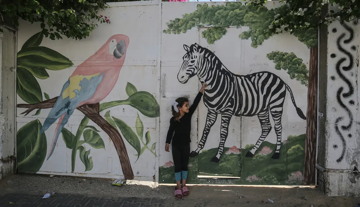 Seorang gadis Palestina menyentuh mural zebra di luar kebun binatang lokal yang ditutup di Rafah di Jalur Gaza selatan (26/5/2020). Kebun binatang itu ditutup selama liburan Idul Fitri karena pandemi virus coronavirus COVID-19. (AFP/Said Khatib)