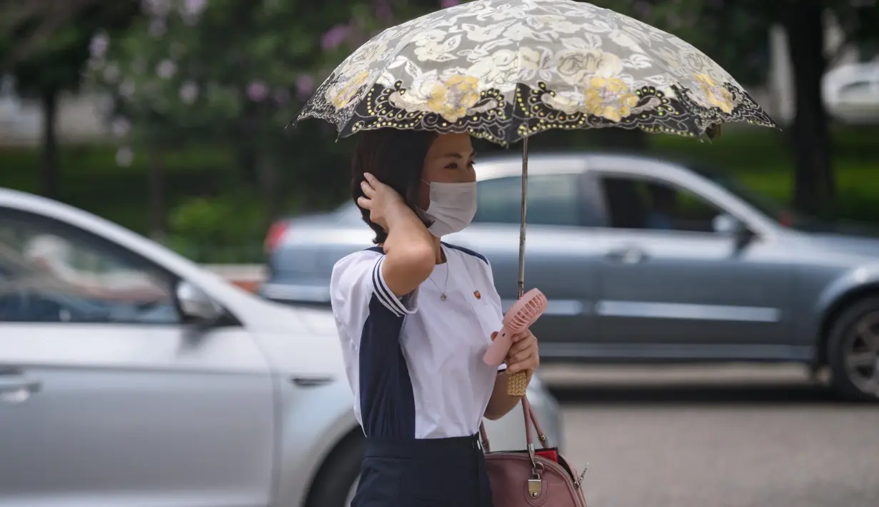 Seorang wanita berlindung di bawah payung saat suhu tinggi mencapai 34 derajat celsius di Pyongyang, Korea Utara, Rabu (21/7/2021). Musim Panas dimulai pada bulan Juni hingga Agustus, dan puncak musim panas adalah bulan Agustus. (KIM Won Jin / AFP)